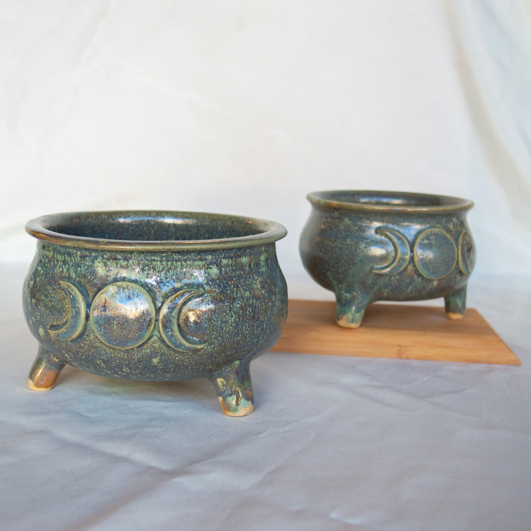 two cauldron planters with goddess mon symbols on a plain background